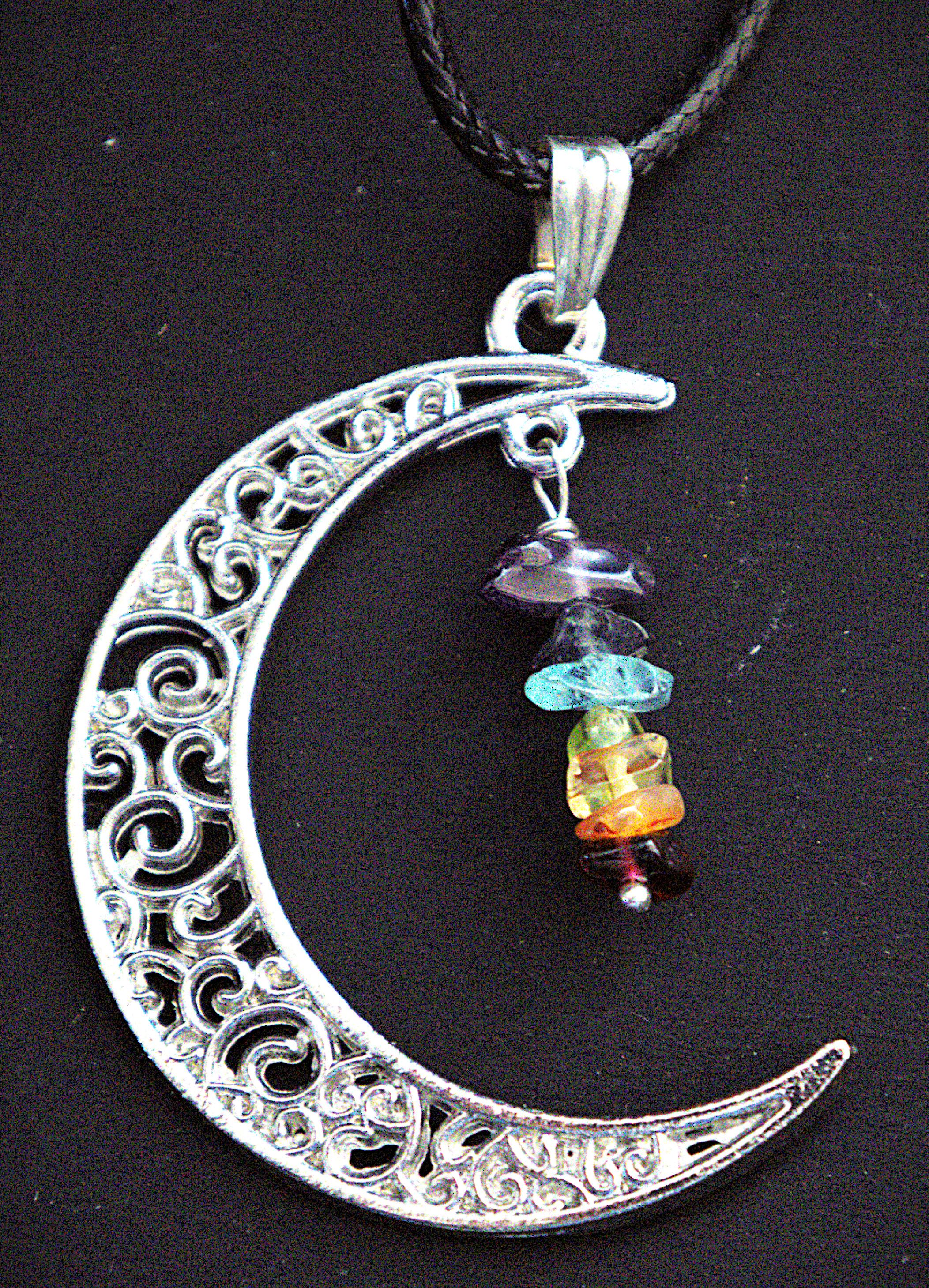 A silver crescent moon pendant necklace with intricate filigree cutouts and a dangling multi-colored gemstone bead charm, shown on a black cord against a dark background.