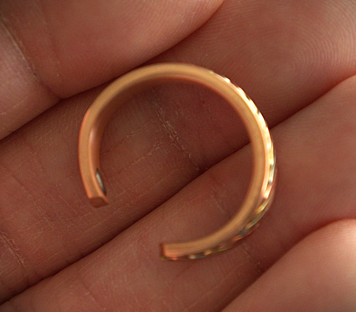 A small open-ended ring in a warm rose-gold tone resting on a person's fingers.