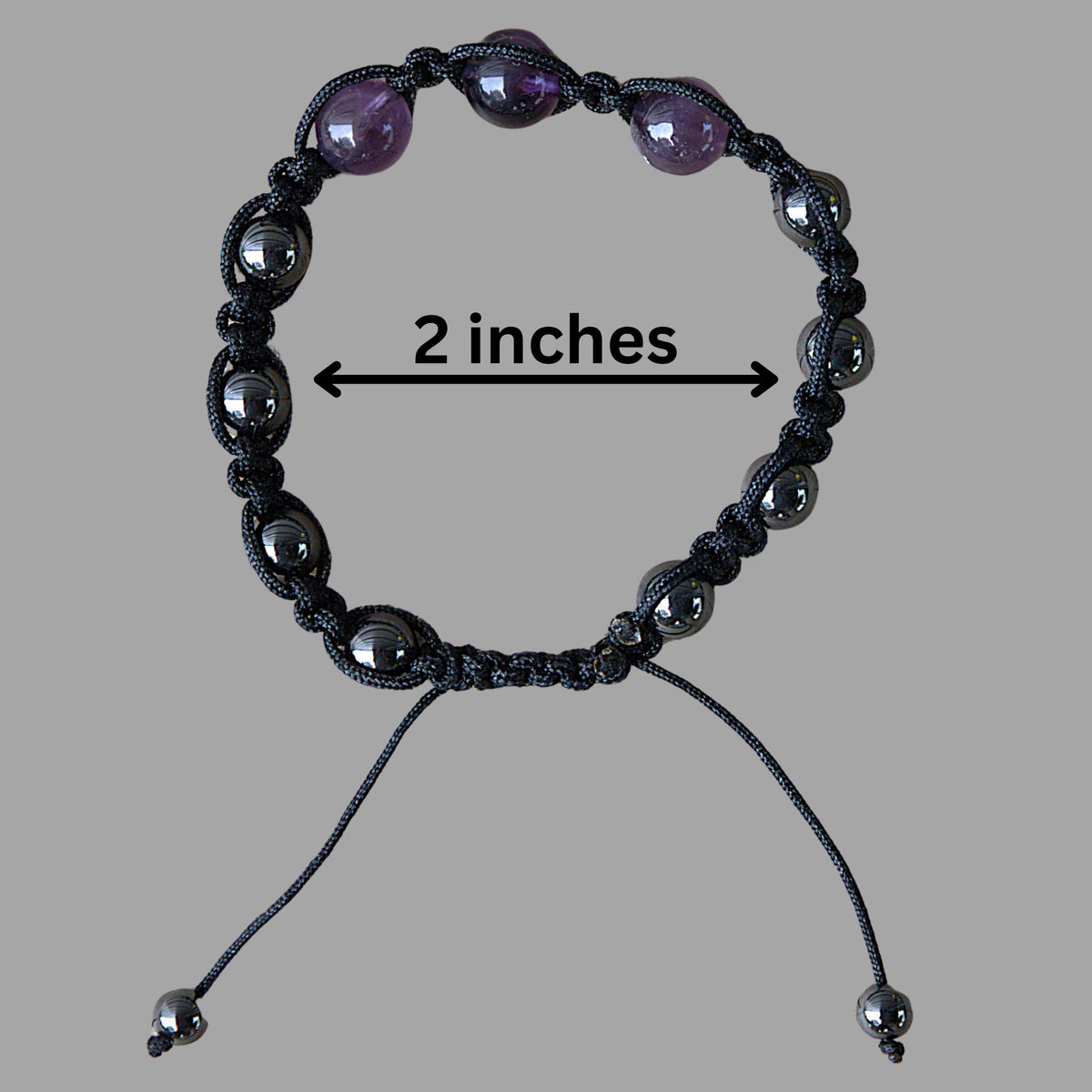 A black macrame bracelet with dark gray metallic beads and three purple amethyst beads, shown on a gray background with a '2 inches' size indicator.