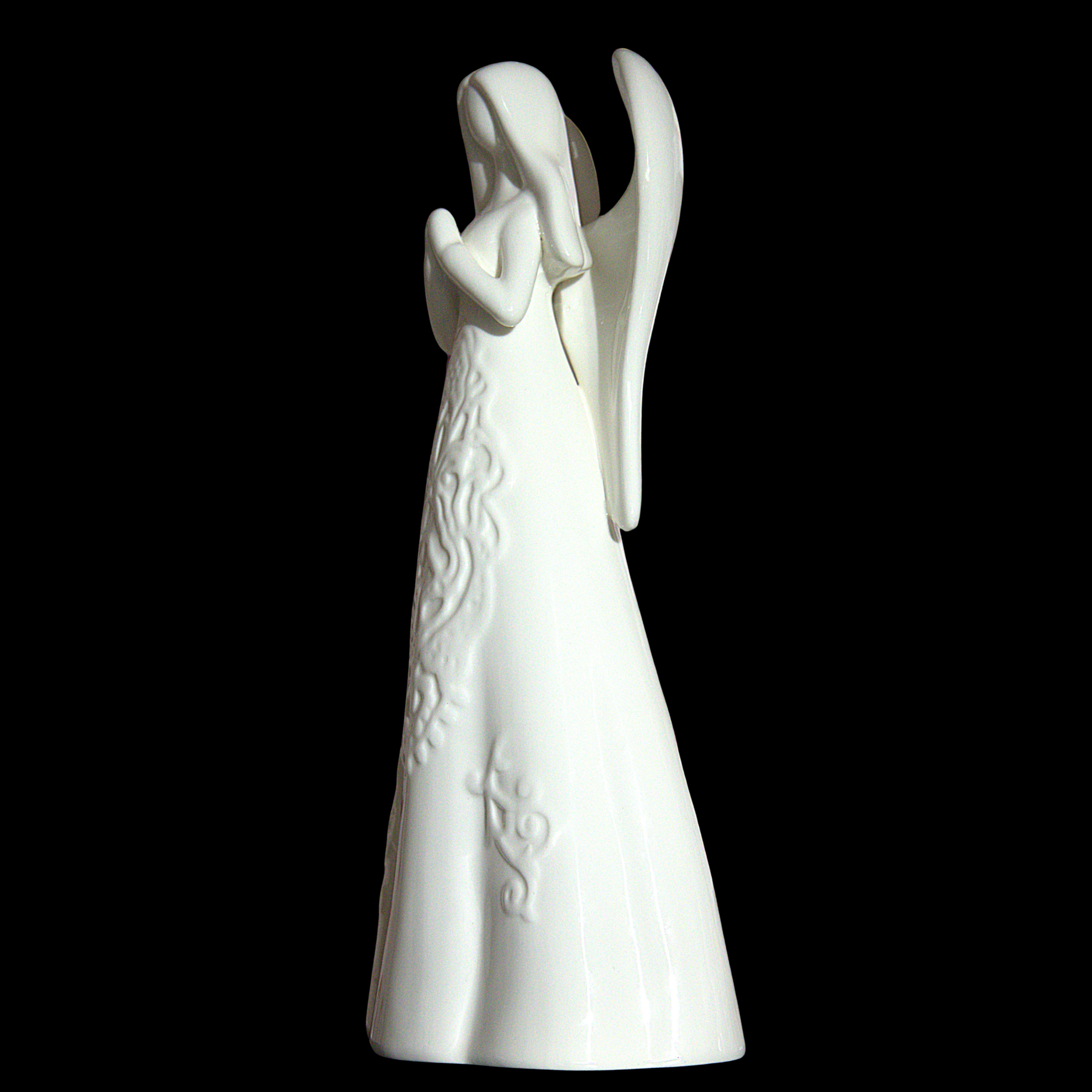 A white ceramic angel figurine with outstretched wings and embossed floral details on its gown, set against a solid black background.