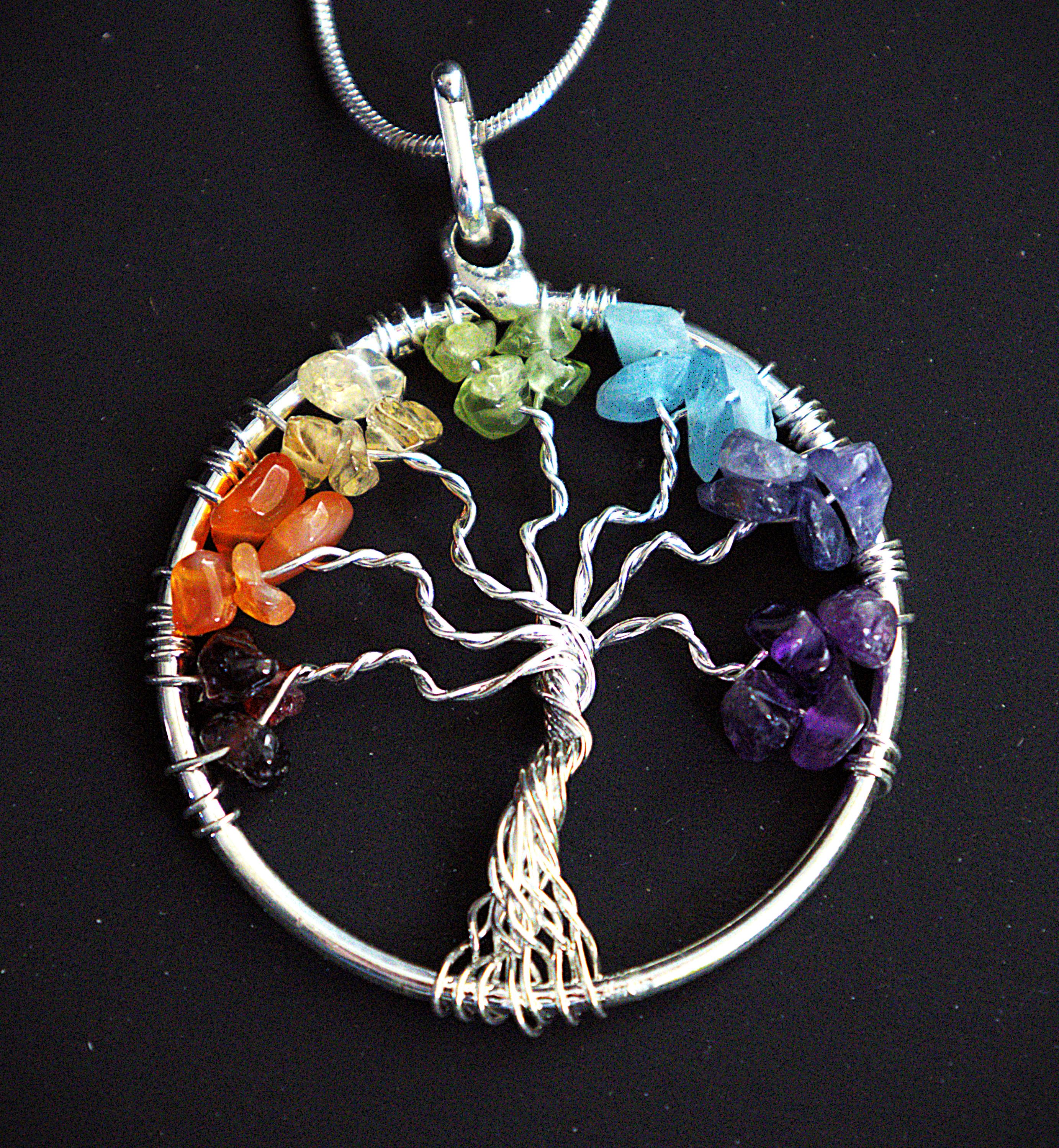 A silver Tree of Life chakra pendant necklace with raw, polished gemstone chips in each of the seven colors, shown on a black background.