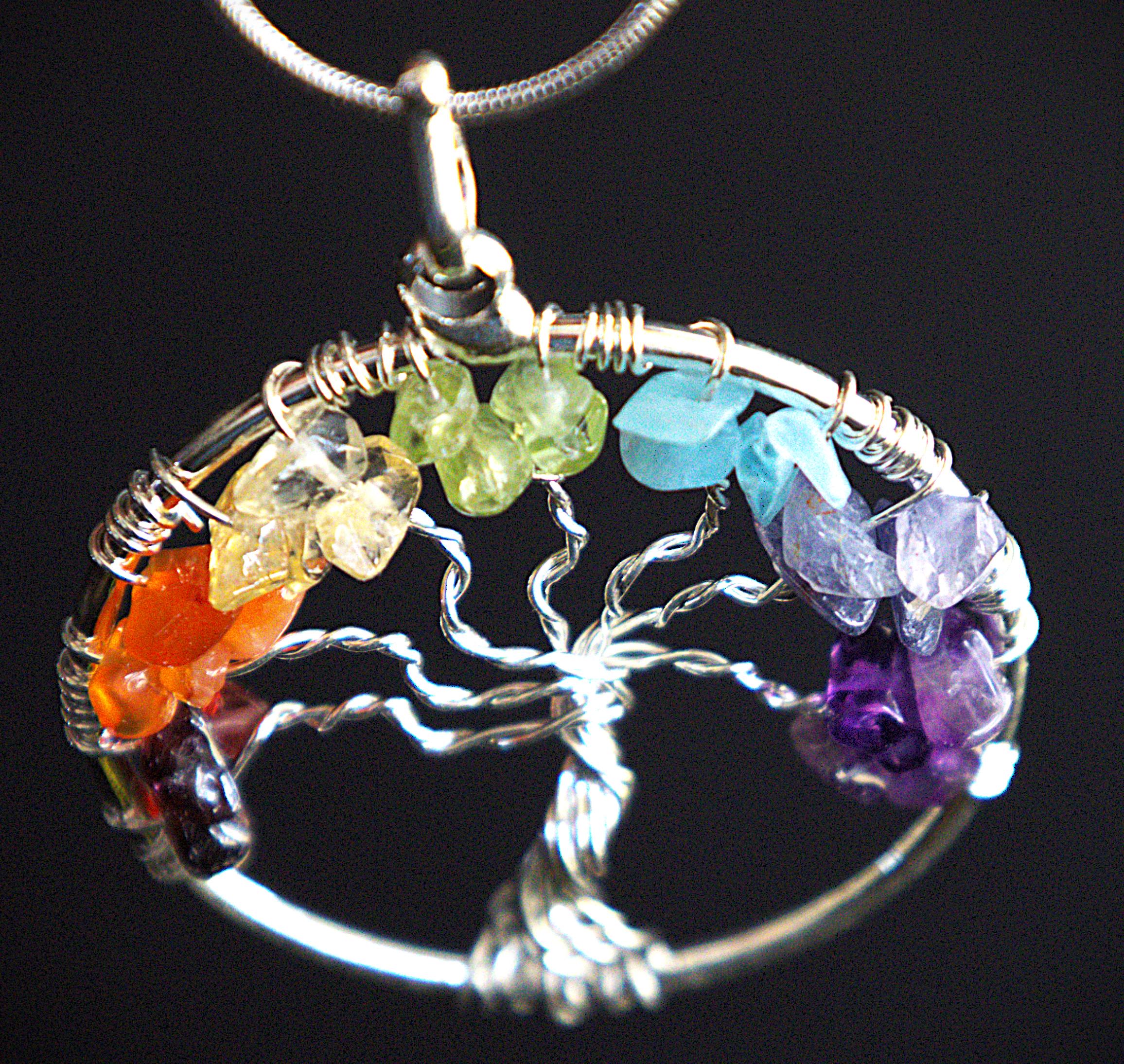 A silver tree of life pendant necklace featuring seven colorful raw gemstone chips in orange, yellow, green, blue, purple, and dark red, set against a solid black background.