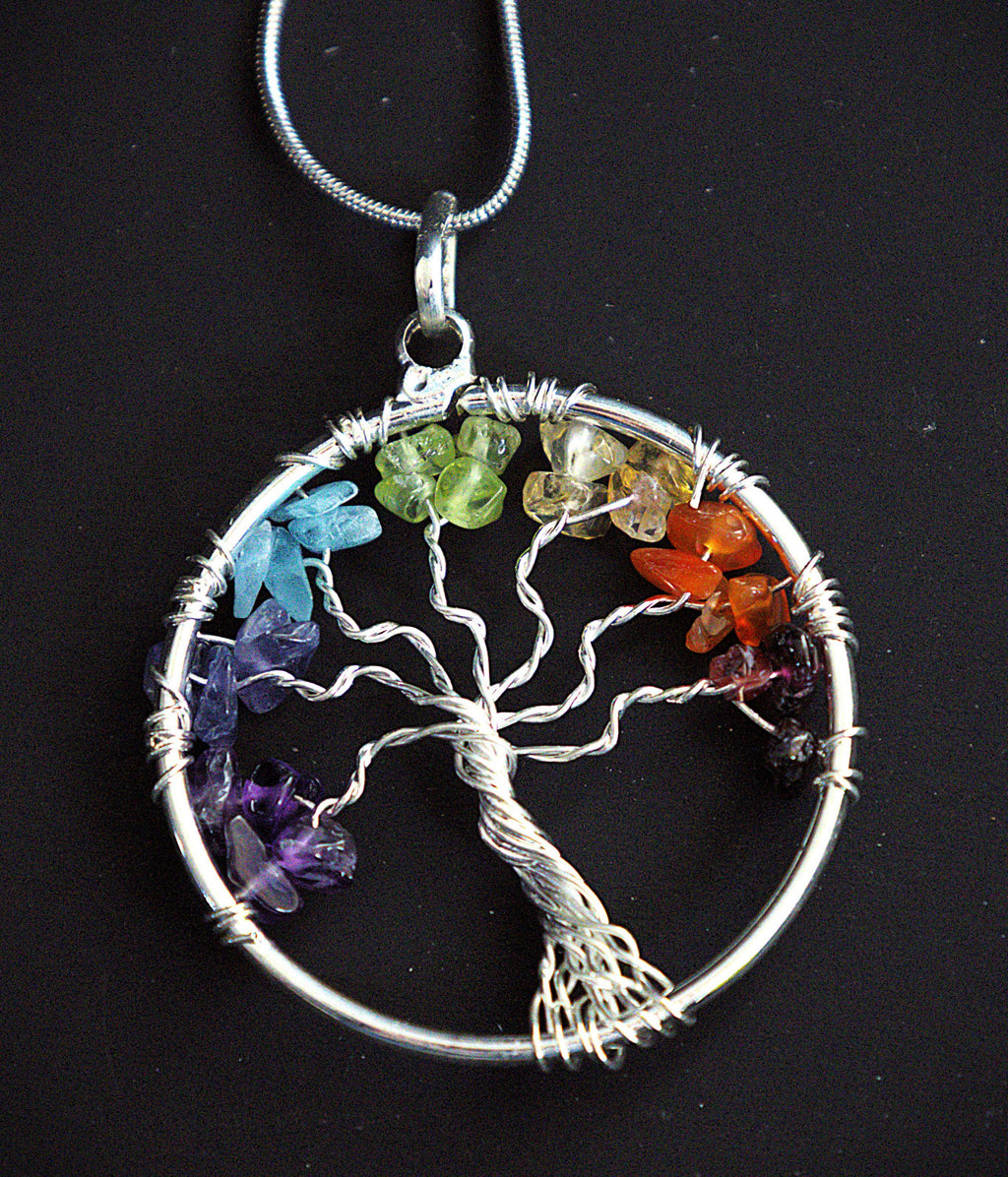 A silver Tree of Life chakra pendant necklace with seven colored gemstone chips in each of the seven branches, hanging from a silver snake chain against a black background.