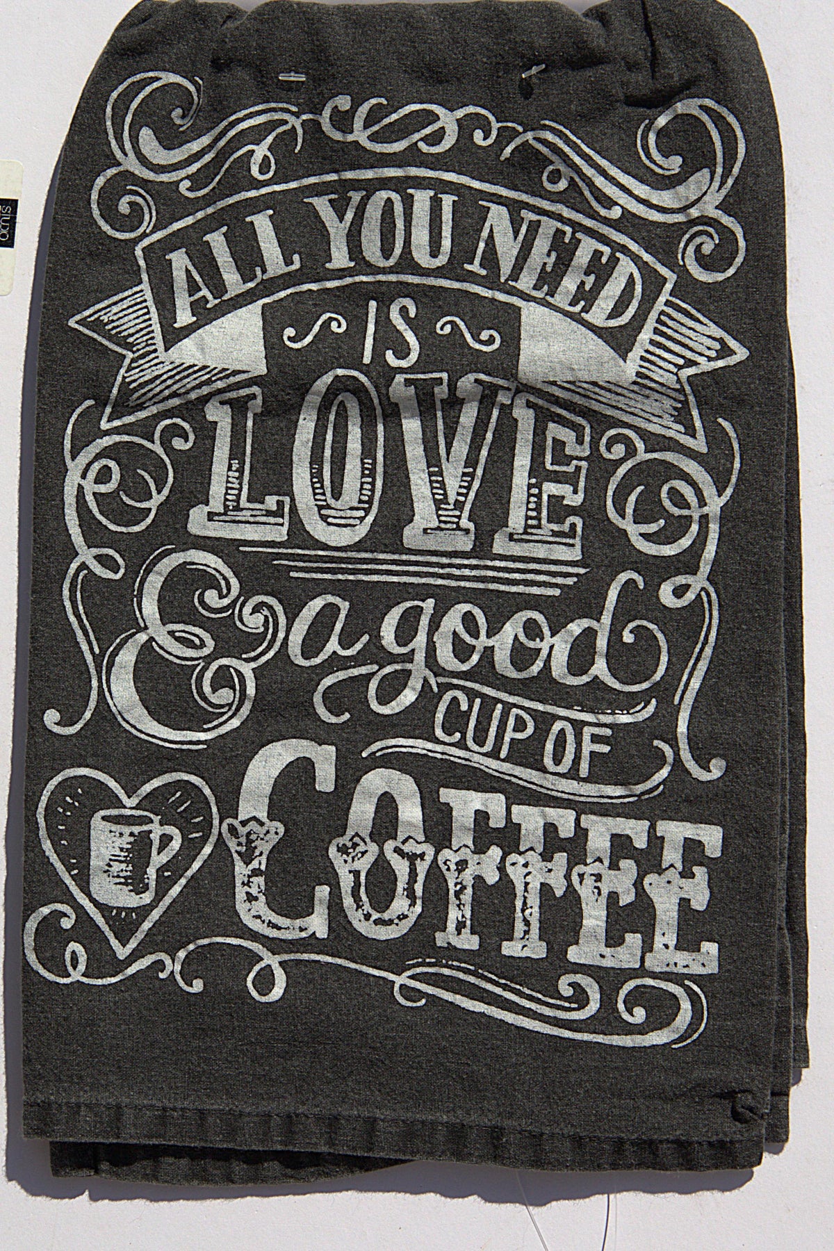 A dark charcoal gray kitchen towel featuring a white hand-lettered graphic that reads 'ALL YOU NEED IS LOVE & a good CUP OF COFFEE' with decorative flourishes and a small coffee cup heart illustration.