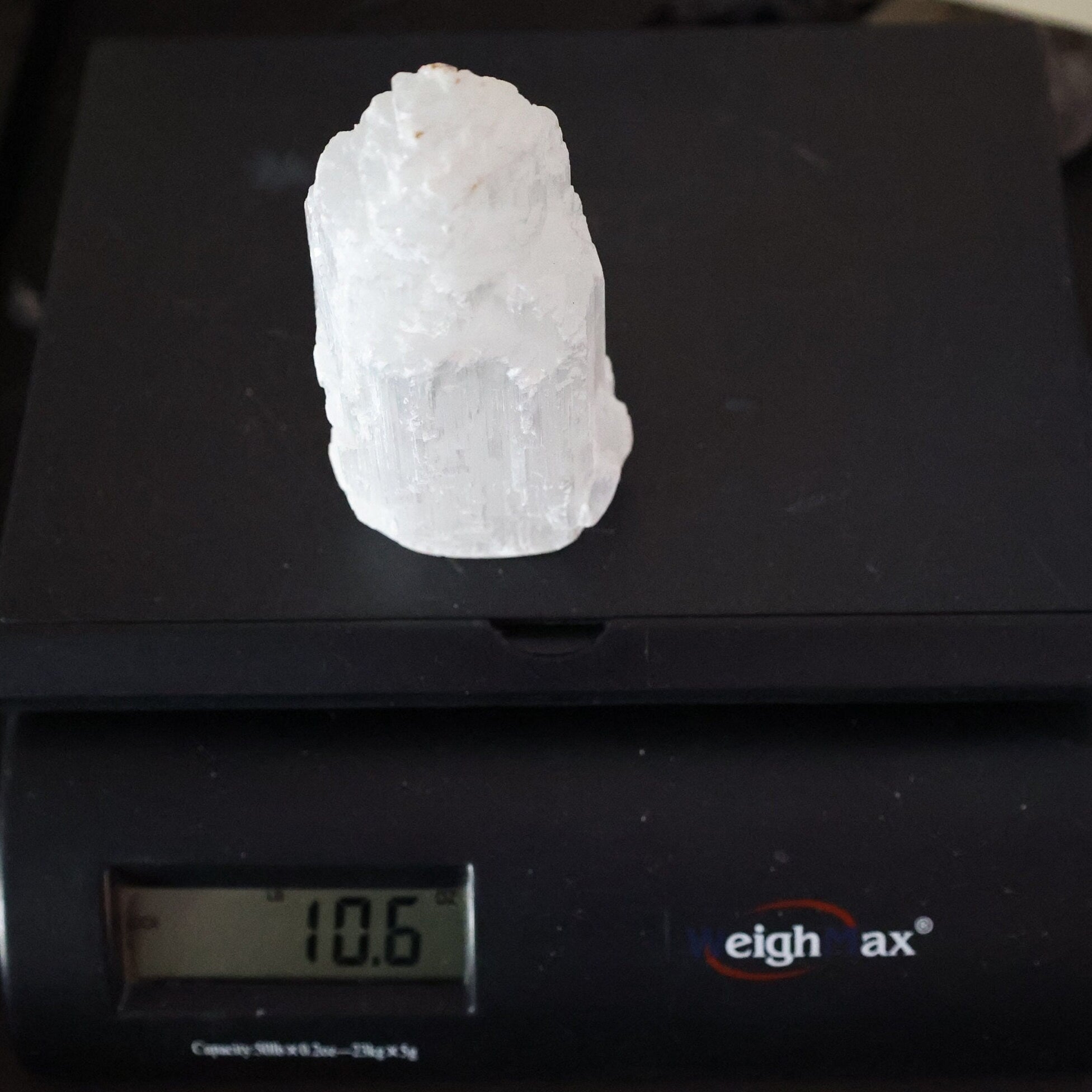 A rough, pale white crystal or mineral specimen sits on top of a black digital scale displaying 10.6 grams.
