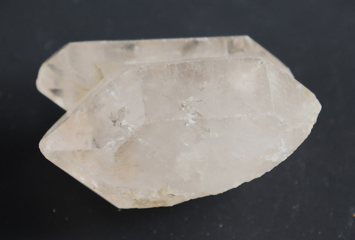 A raw, unpolished crystal cluster with two prominent pointed facets, showing natural translucency and internal inclusions, photographed against a dark, solid background.