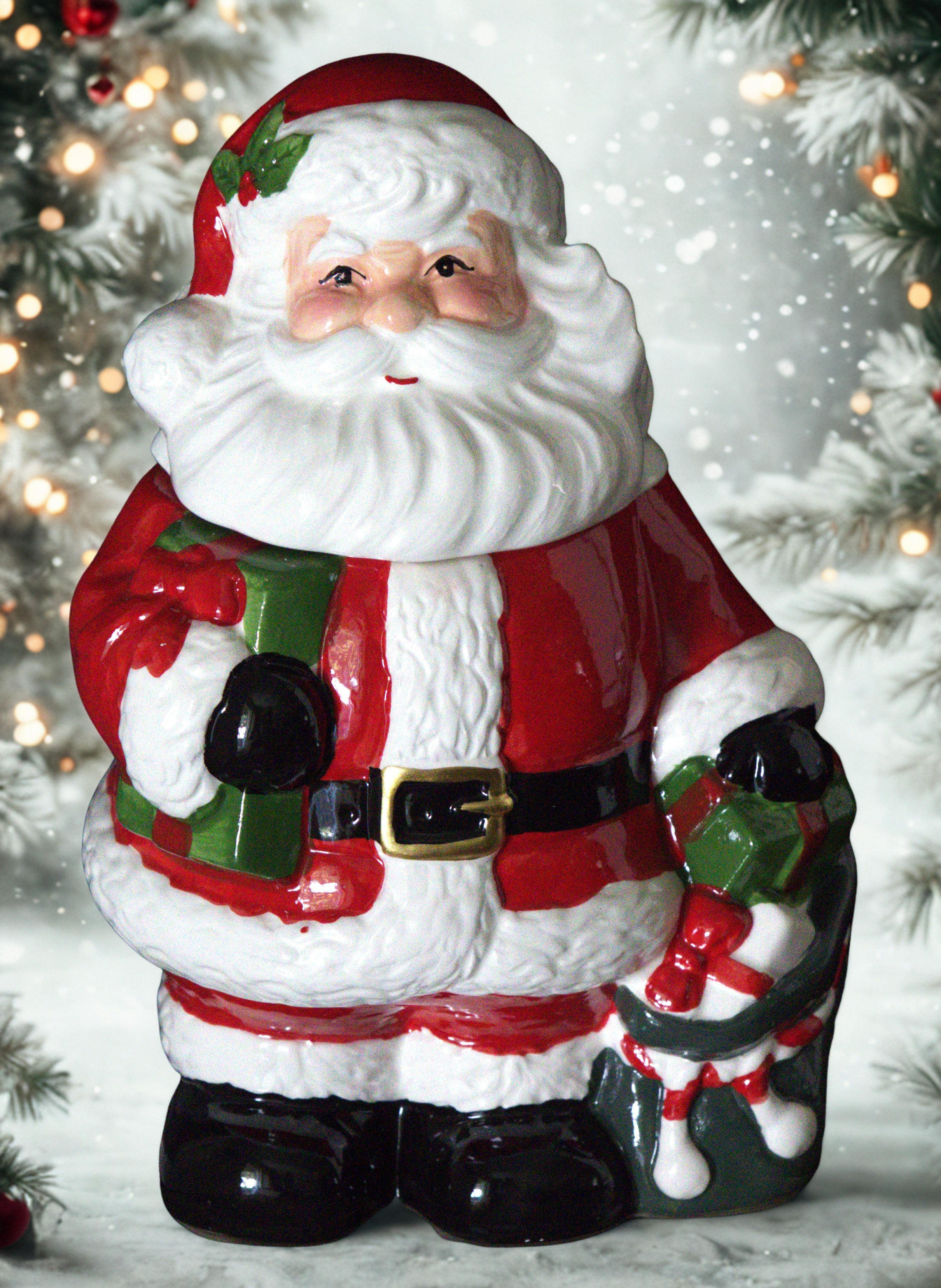 A ceramic Santa Claus figurine holding a green gift box and a decorated sack, set against a snowy holiday background with blurred Christmas trees and lights.