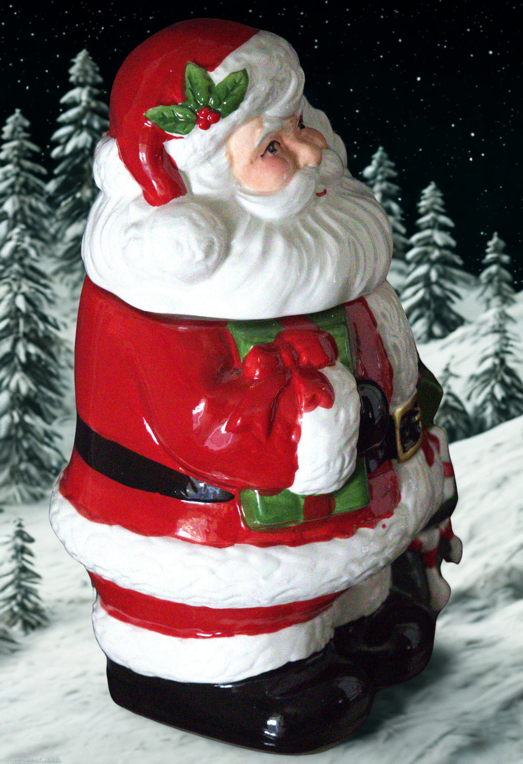 A Santa Claus figurine or cookie jar styled with a snowy forest background, featuring a red and white suit, black belt and boots, and a green holly accent on the hat.