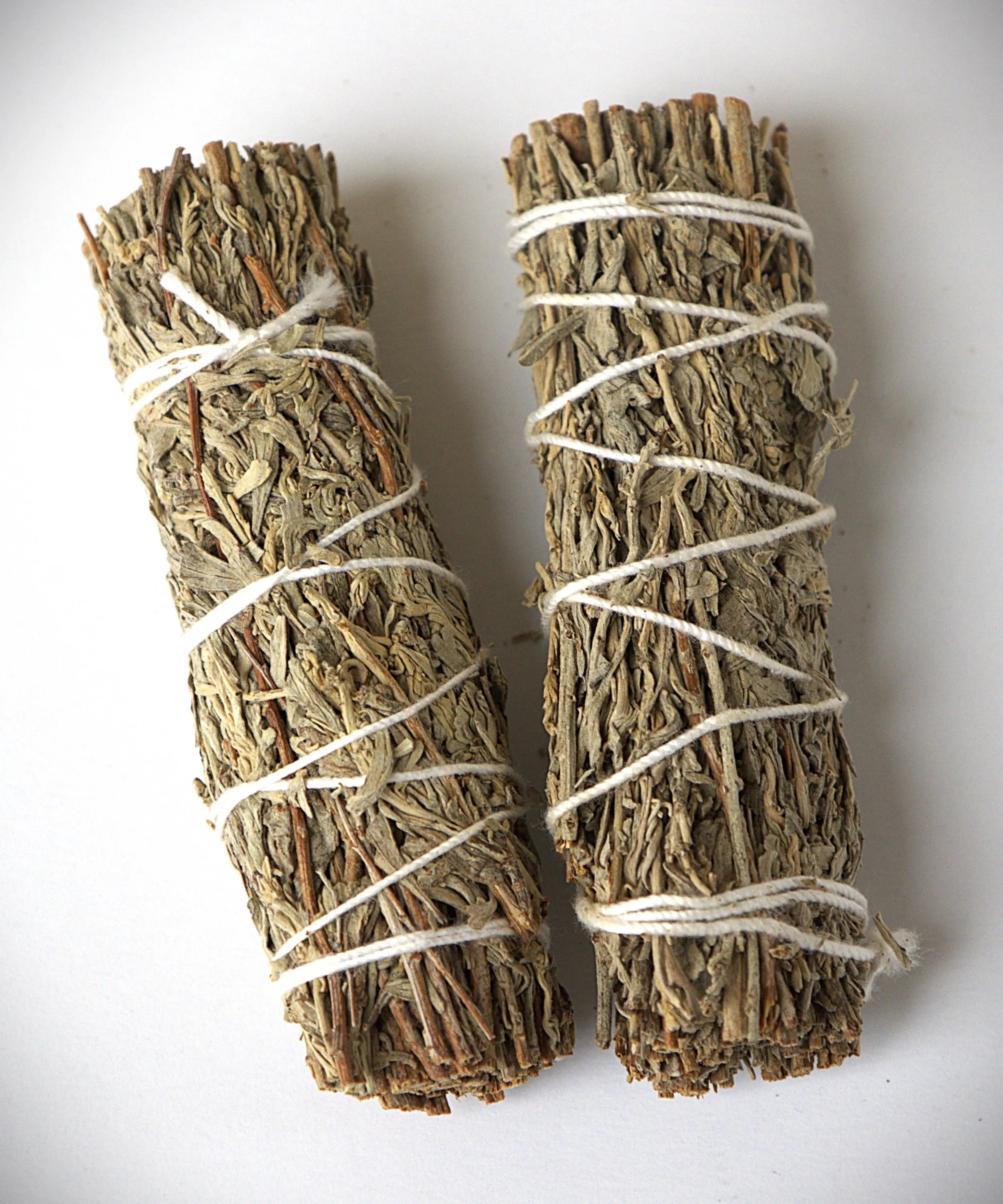 Two dried herb smudge bundles wrapped in white string, photographed on a plain white background.